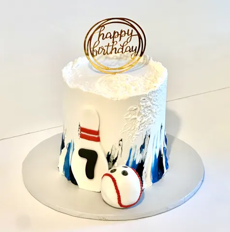 White cake with a bowling pin, a baseball, a number 7, blue textured icing and a gold ring Happy Birthday topper.