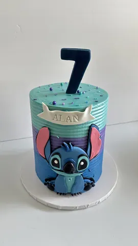 Striped 7th birthday cake in teal, purple and blue with a cute blue character, a name banner and a tall number 7.