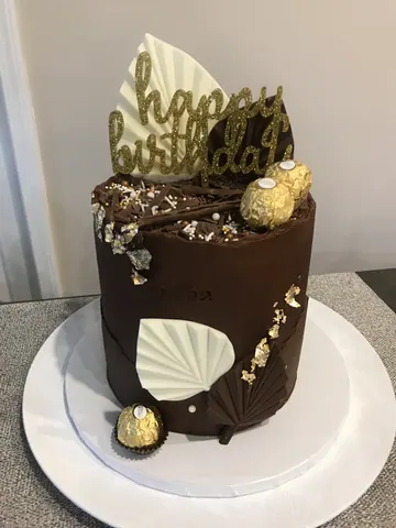 Chocolate cake with chocolate drip, white chocolate fans, chocolate bonbons, gold leaf and a gold Happy Birthday topper.
