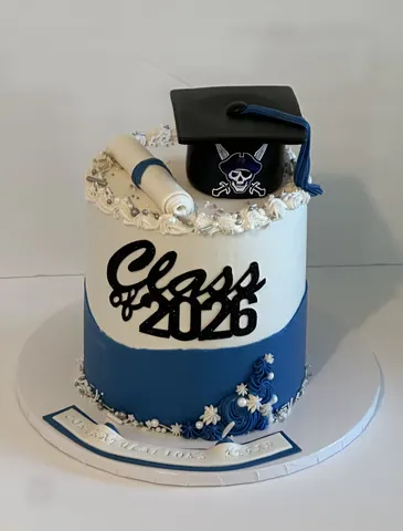 Graduation cake with a blue wave bottom, white top, black Class of 2026 lettering, a diploma and a black grad cap.