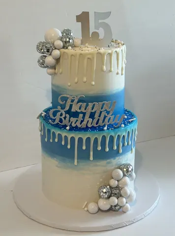 Two-tier 15th birthday cake with blue ombre, white drips, silver disco balls, pearls and a silver 15 topper.