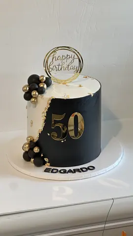 Black and white split cake for a 50th birthday with a gold 50, gold and black spheres and a gold ring topper.