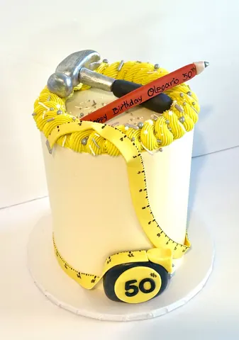 Cream 50th birthday cake wrapped in a yellow tape measure with a sugar hammer and pencil on top.