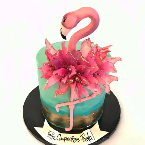 Teal ombre cake with a gold base, a large pink sugar flower and a pink flamingo standing on top.
