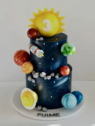 Two-tier midnight blue galaxy cake with painted stars, sugar planets, a rocket, a silver asteroid belt and a sun with the number 3 on top.