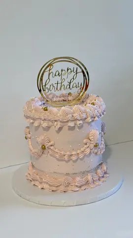 Tall pale pink vintage cake with swags of piped buttercream, pearl details and a gold ring Happy Birthday topper.