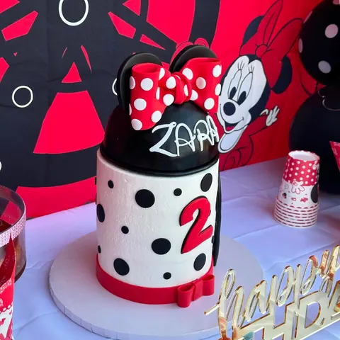 White and black polka-dot 2nd birthday cake with a big red number 2, black mouse ears, a red polka-dot bow and a name on top.