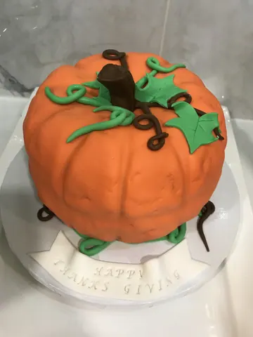 Cake sculpted as an orange pumpkin with a brown stem, curling vines and green leaves for Thanksgiving.