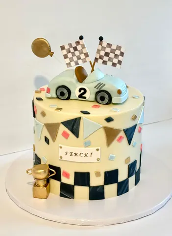 Cream 2nd birthday cake with a race car on top, checkered flags, colorful bunting, a checkered base and a gold trophy.
