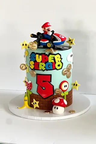 Colorful 5th birthday cake with a go-kart racer figure, gold coins, stars, a red mushroom and a brick pattern base.