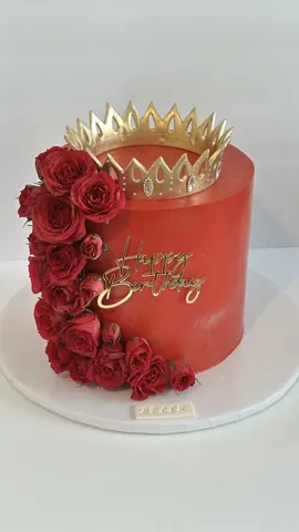 Deep red cake with a cascade of red roses, a gold crown on top and a gold script Happy Birthday sign.