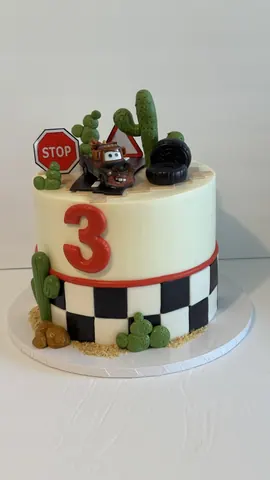 Cream 3rd birthday cake with a red number 3, a checkered band, sugar cactus, a stop sign and a tow truck figure.