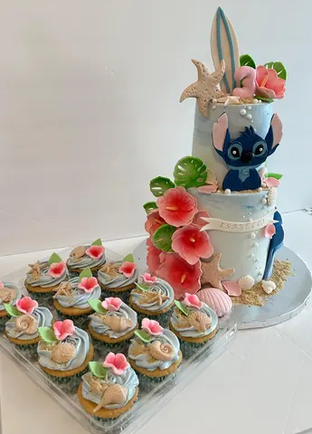 The tropical beach cake next to a tray of matching cupcakes with pink flowers and sugar sea shells.