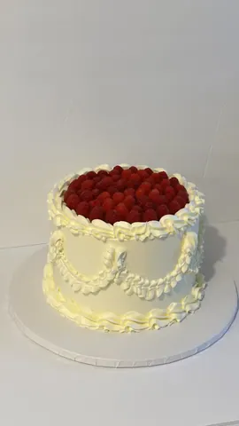 White vintage cake with piped garlands and a crown of fresh raspberries on top.