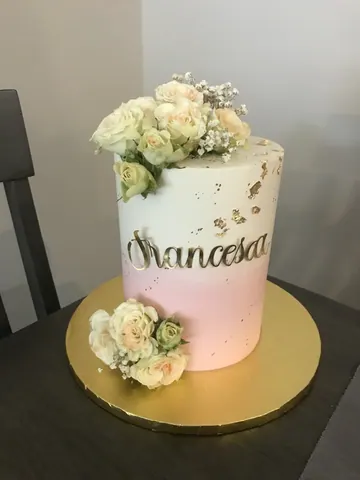 White to pink ombre cake with cream roses, gold flakes and a gold script name.