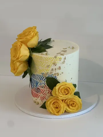 White cake with fresh yellow roses, a colorful stenciled chevron pattern and gold flakes.